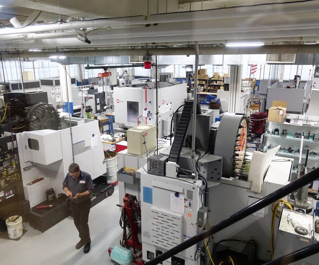 A business buyer reviewing financial documents inside a modern small manufacturing facility, with machinery in the background and subtle BusinessOwner.com branding on a tablet screen.