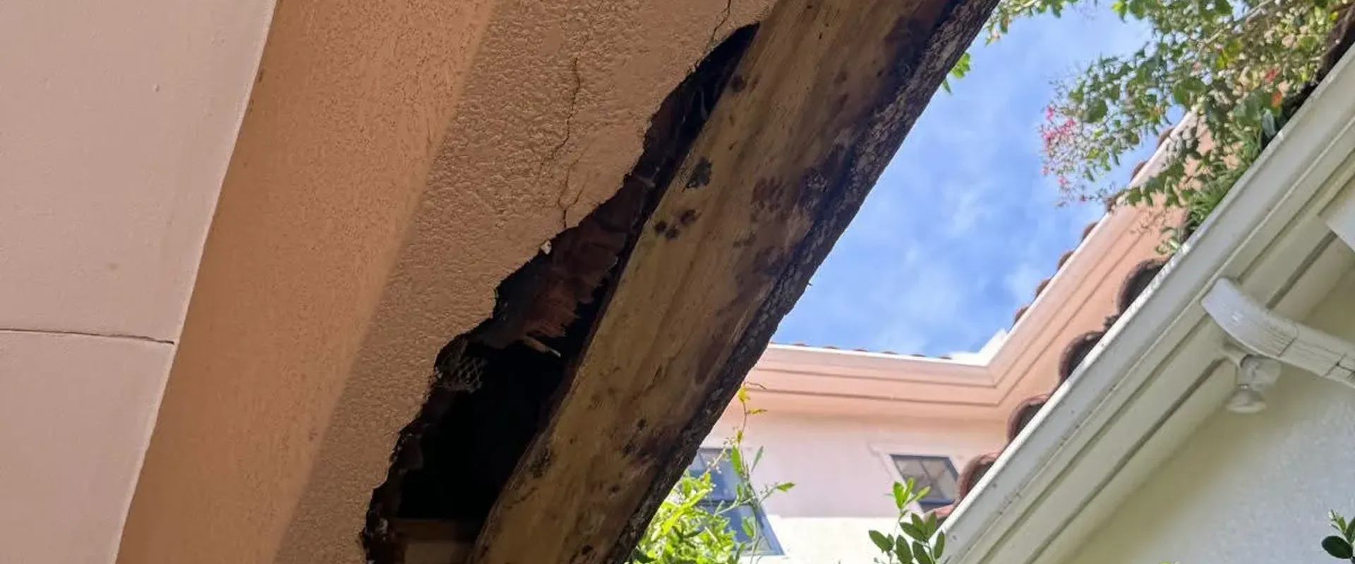 Severe wood rot exposing rafters through stucco, dramatic before shot of structural damage