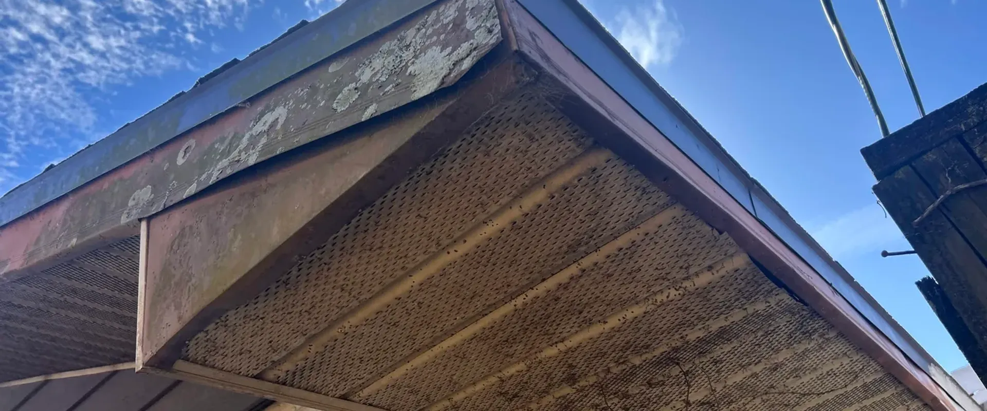 Severely weathered and rusted vented soffit at a gable end with peeling paint