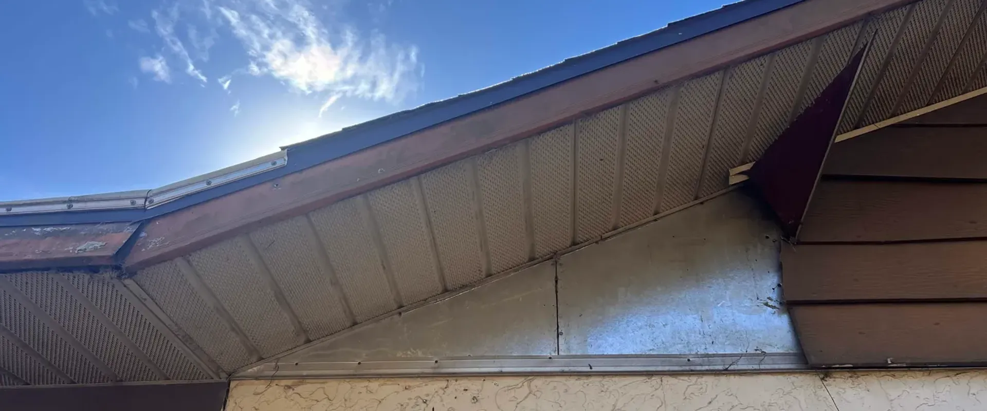Dirty old vented soffit at a sloped gable showing weathered brown discoloration