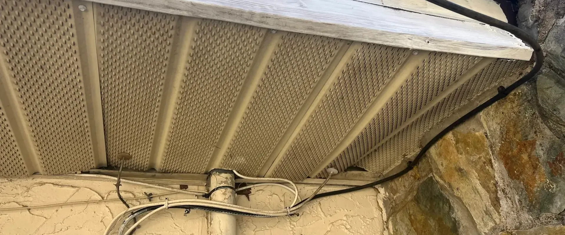 Dirty old vented soffit with hanging wires and weathered wall surfaces