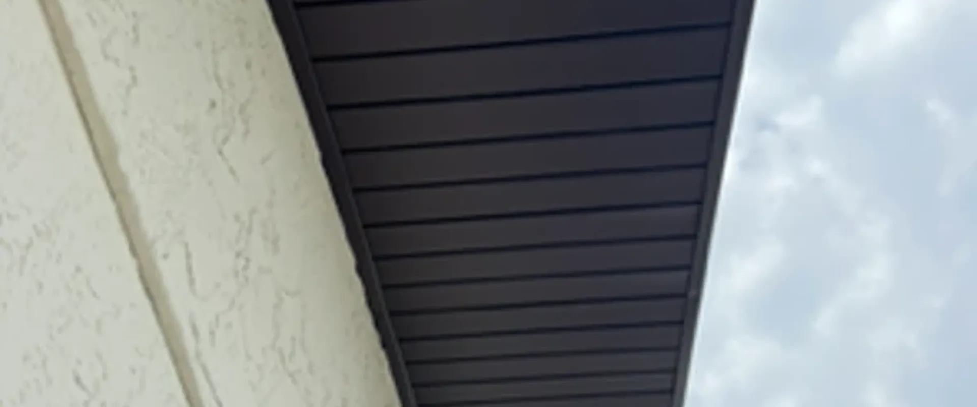 Dark brown Mastic hidden-vent soffit shown in profile at a cream stucco column, showcasing the seamless smooth panel finish