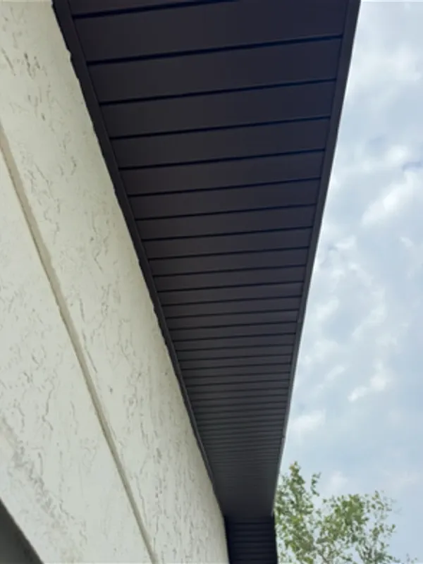 Dark brown Mastic hidden-vent soffit shown in profile at a cream stucco column, showcasing the seamless smooth panel finish