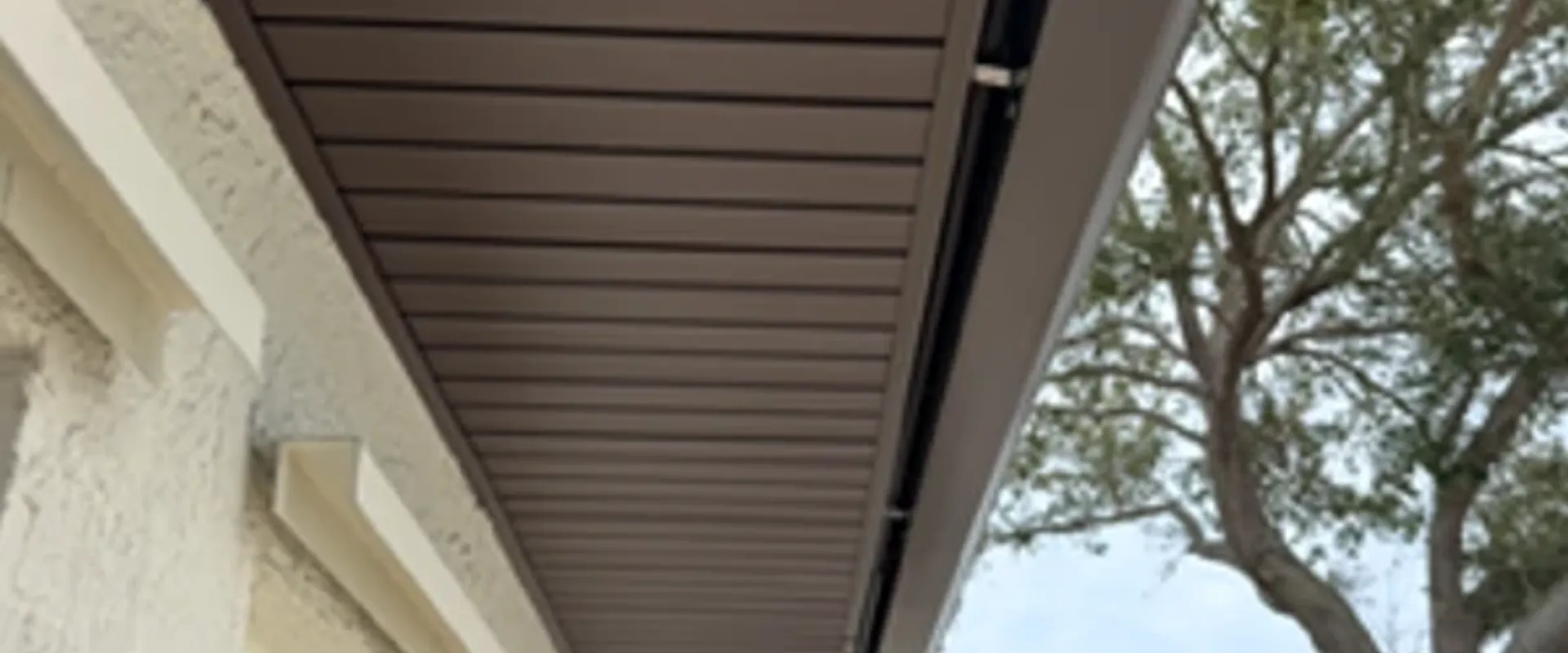 Dark brown Mastic hidden-vent soffit underside view at the eave of a Tampa Bay home, showing premium concealed ventilation