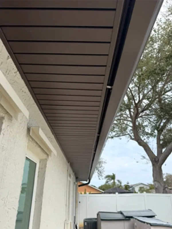 Dark brown Mastic hidden-vent soffit underside view at the eave of a Tampa Bay home, showing premium concealed ventilation