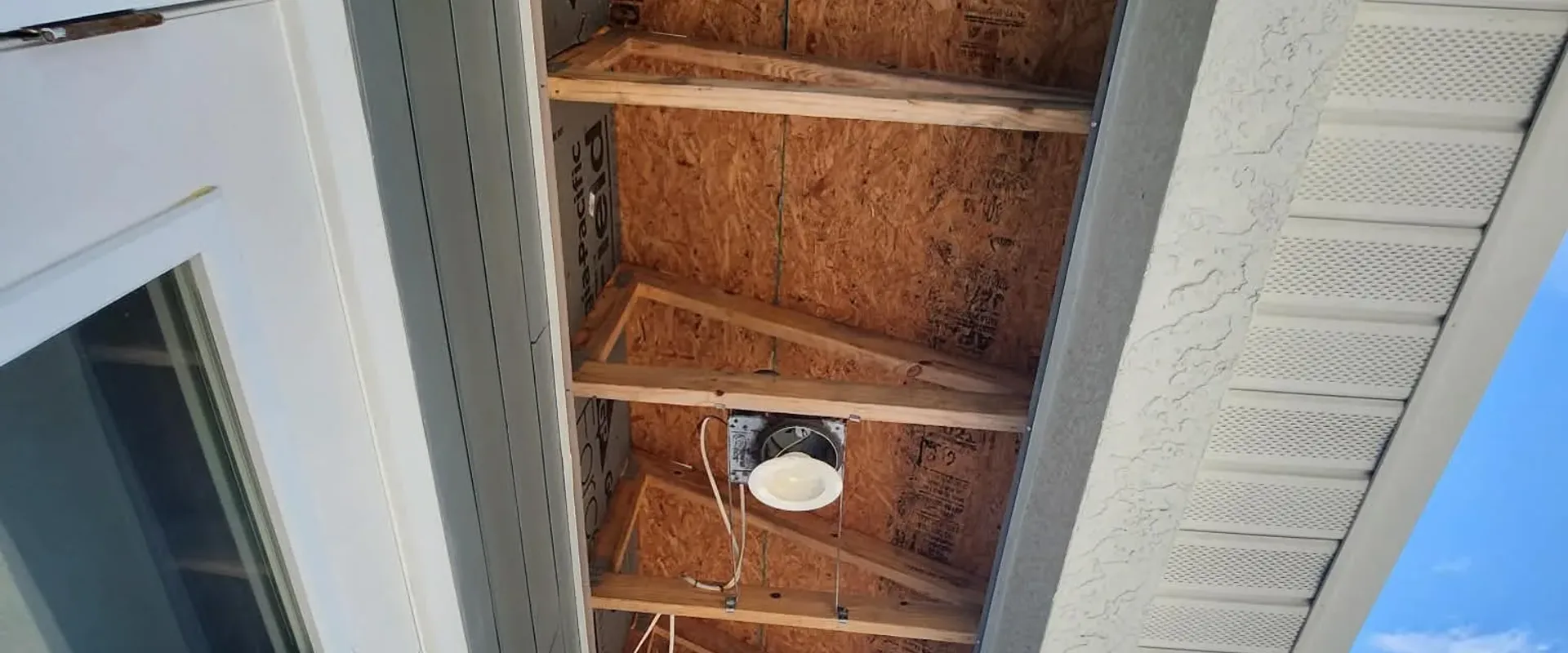 Exposed rafter framing and new sheathing during a soffit and fascia repair, demonstrating the rotted wood replacement before aluminum wrap installation