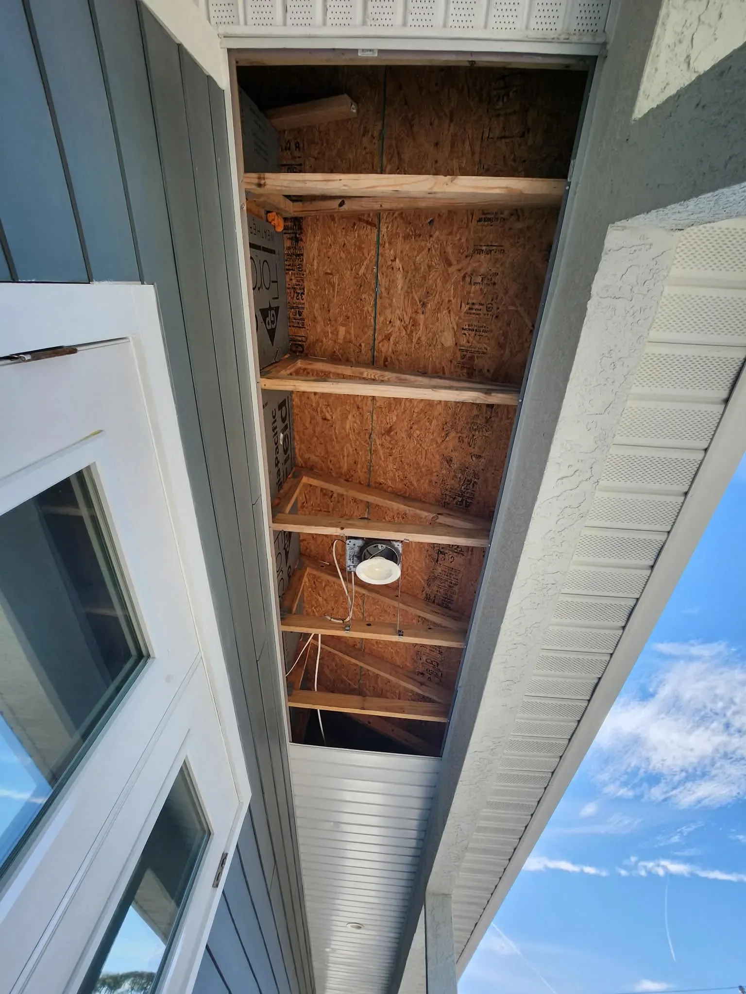 Exposed rafter framing and new sheathing during a soffit and fascia repair, demonstrating the rotted wood replacement before aluminum wrap installation